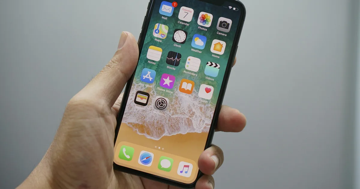 A hand holding an iPhone showing the iOS home screen