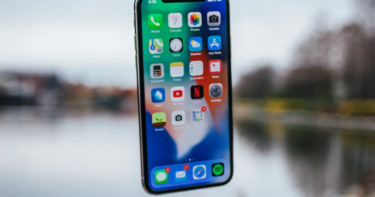 An iPhone held up showing its home screen, outdoors