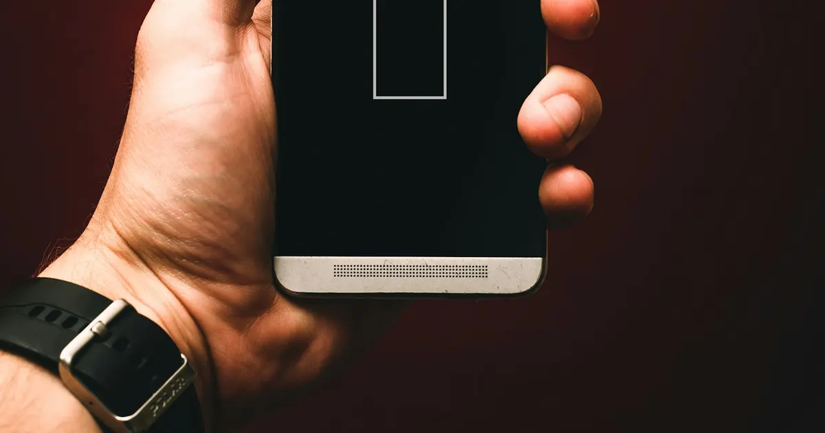 Hand holding a phone showing a low battery icon, a common companion of overheating
