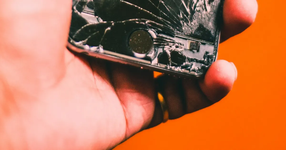 Hand holding an iPhone with a badly cracked screen
