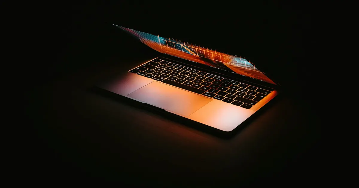 MacBook glowing half-open on a black surface