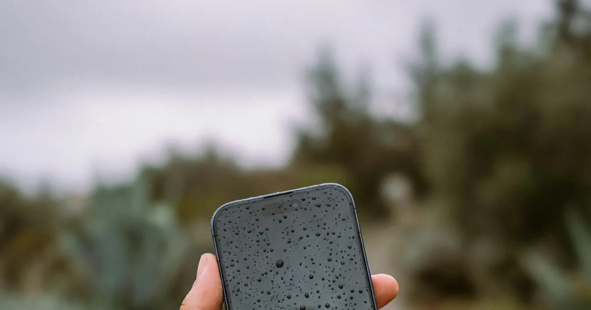 Hand holding a rain-soaked smartphone, representing liquid damage