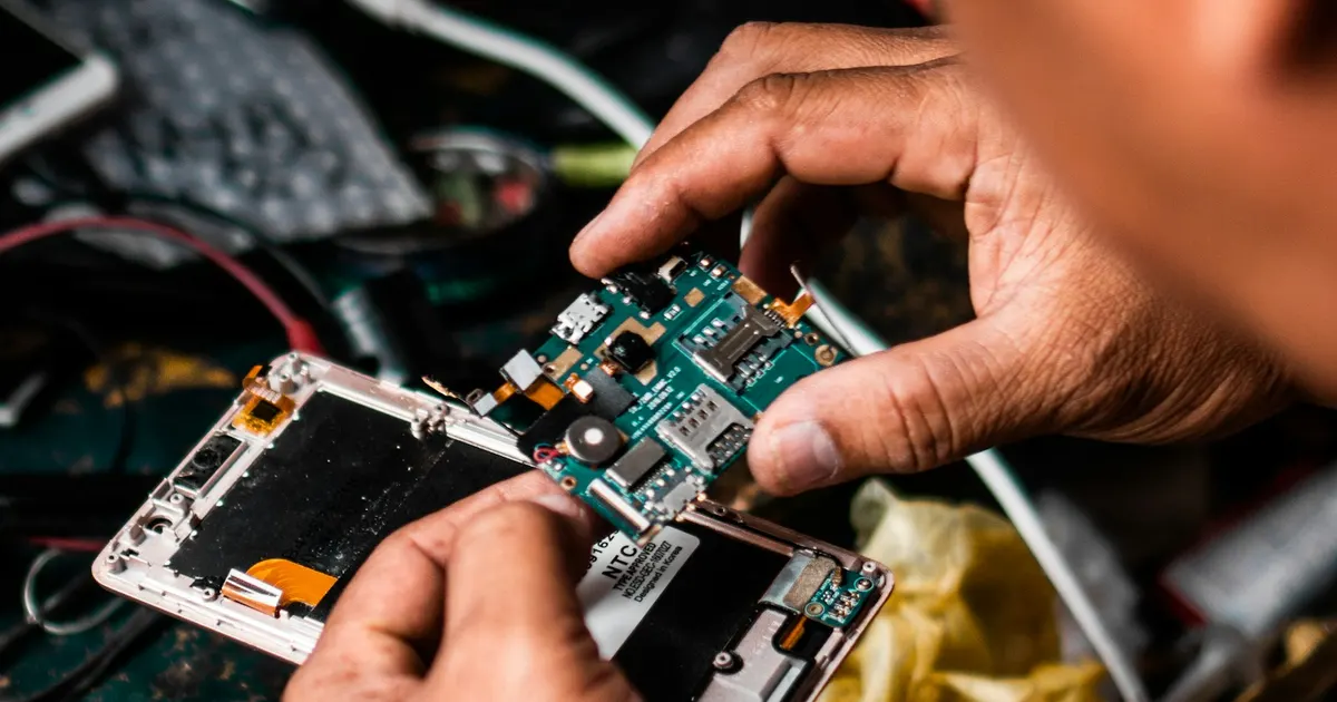 Technician's hands repairing a device logic board at a workbench